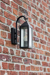 Classic black outdoor wall lantern with clear glass panels illuminating a rustic red brick wall. Perfect for exterior home lighting and architectural detail.