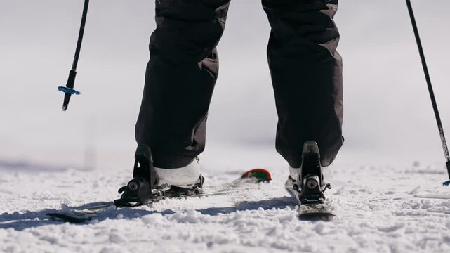 Skier standing on a snowy slope preparing to ski downhill on a sunny winter day. Perfect for themes of winter sports, adventure, and outdoor freedom.