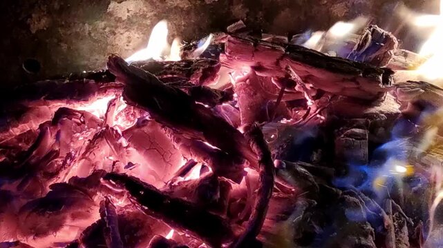 Hot coals in a fire. Late evening, dark outside. The firewood is dying down, leaving only bright red embers. The coals glow and shimmer in the light breeze, with tongues of flame rising above them.