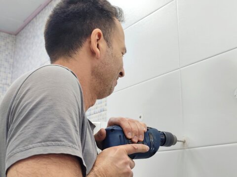 Man drilling a hole in the tile of bathroom