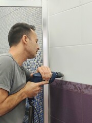 Man drilling a hole in the tile of bathroom