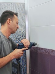 Man drilling a hole in the tile of bathroom