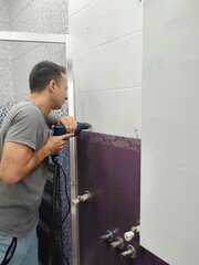 Man drilling a hole in the tile of bathroom