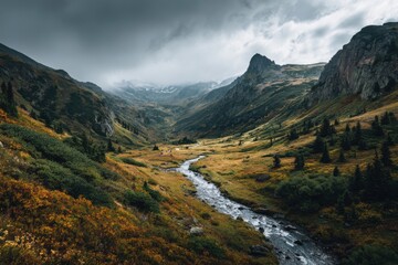 Fototapeta premium Picturesque mountain landscape with meandering river, golden-green valley, dramatic clouds, and snow-capped peaks, capturing the essence of autumn's beauty and nature's majesty