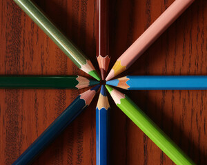 Vibrant colored pencils arranged in a dynamic starburst pattern on a rich wooden surface, symbolizing creativity and collaboration
