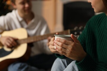 Man playing guitar for his beloved woman in room, selective focus