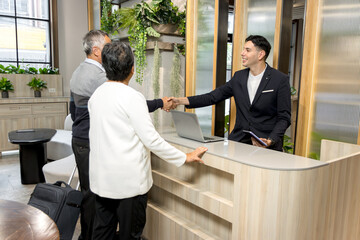 Happy senior Asian couple checking in at hotel on holiday vacation with young male receptionist....