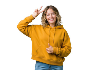 Young woman wearing a yellow hoodie and jeans, making a peace sign and giving a thumbs up, isolated on transparent background