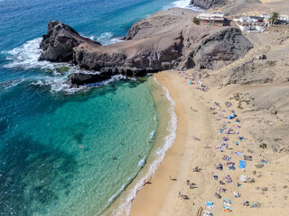 Aerial view of Playa de Papagayo in Lanzarote, featuring a crescent-shaped golden beach surrounded by rocky cliffs and turquoise water.