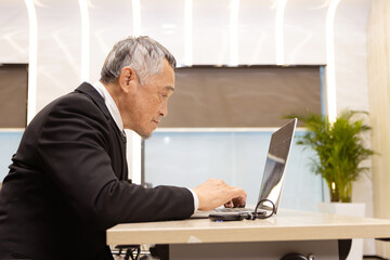 Serious Asian senior businessman in suit typing on laptop at working desk. Elderly successful male boss work on laptop computer at office workplace. Asian mature man business worker with technology.