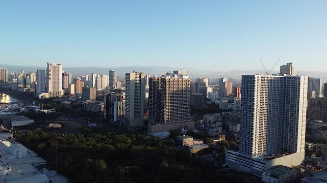 Aerial drone view of Pasay City skyline during golden hour showing modern high-rise buildings, condominiums, and urban development in Metro Manila, Philippines, with clear blue sky and city landscape.