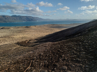 Aerial view of volcanic cones and arid landscape on La Graciosa Island, Canary Islands, with distant views of surrounding islands and the Atlantic Ocean.
