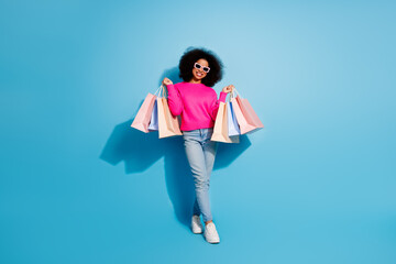 Young woman in trendy outfit holds shopping bags and smiles against a blue background showcasing casual and stylish vibes