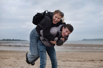 The husband and wife have fun together, they have been married for 25 years and they always have a good time together. Two friends share a playful piggyback ride on sandy beach, laughing