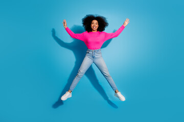 Obraz premium Cheerful young woman in a bright pink top smiling and jumping against a blue backdrop, expressing joy and vibrance