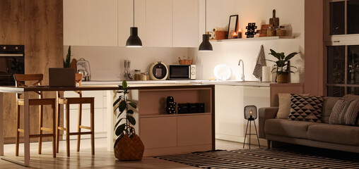 Interior of modern kitchen with counters, table and glowing lamps at night