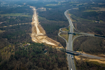 Construction crews work on a high-speed train line in France, creating a path through the landscape while a highway runs parallel.