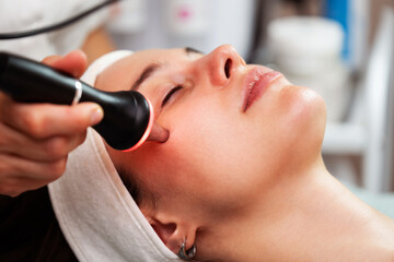 Woman receiving modern ultrasound anti-aging facial treatment in a clinic, esthetician using device for skin tightening and rejuvenation, promoting glowing, youthful complexion