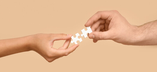 Hands of loving young couple with puzzle pieces on beige background