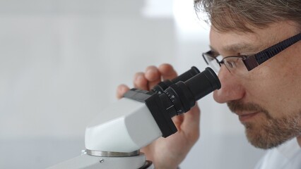 Close up of a male scientist looking through a microscope, conducting research and analysis in a laboratory setting, showcasing scientific investigation and discovery. Medicine and science concept