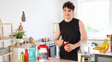 Sporty young man with protein powder at table in kitchen