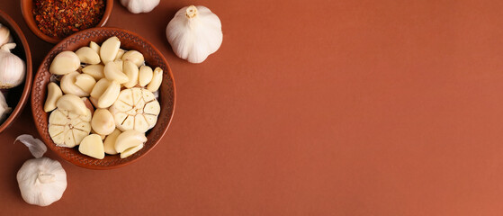 Bowl with fresh garlic cloves and spices on brown background