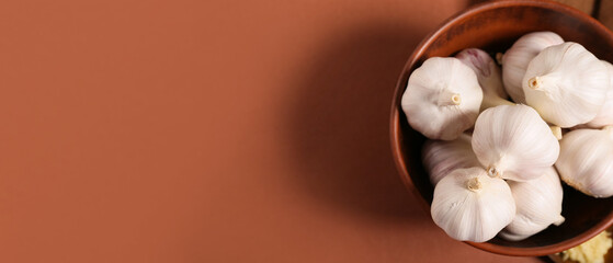 Bowl with fresh garlics on brown background