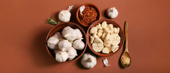 Bowls with fresh garlics and rosemary on brown background