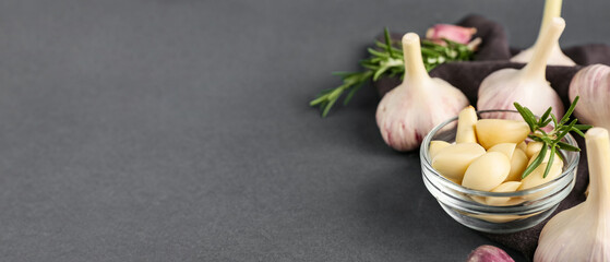 Glass bowl with fresh garlic cloves and rosemary on grey background, closeup