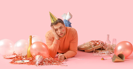 Young man with hangover and balloons lying after Birthday party on pink background