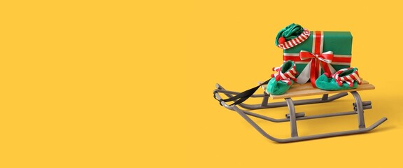 Sled with Christmas gift and elf clothes on yellow background with space for text