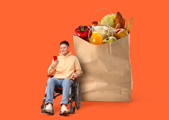 Young man in wheelchair with mobile phone on orange background