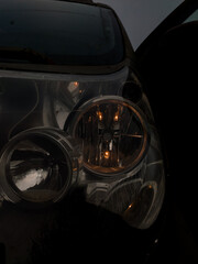 Close-up of a car's round, reflective headlight and turn signal glowing amber in the deep twilight or dark, conveying mystery, travel, or late-night driving.