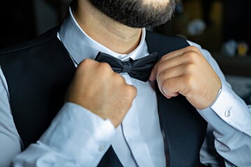 A man with a beard adjusting his black bow tie