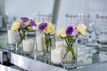 A glass vase with a bouquet of purple and yellow roses and white candles