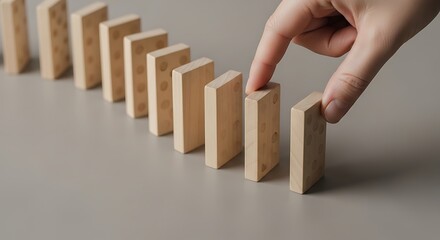Strategic hand carefully places final domino, symbolizing decisive action, risk, or the tipping point of a planned sequence leading to inevitable consequences.