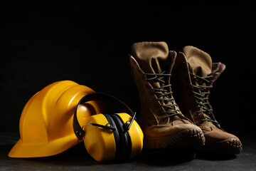 Hardhat, protective earmuffs and boots on black background, closeup