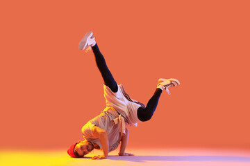Handsome young man dancing hip-hop on orange background