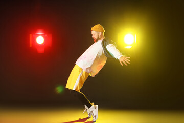 Handsome male hip-hop dancer dancing on dark color background