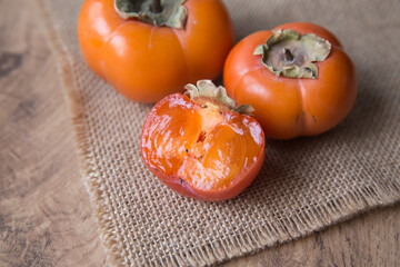 Whole and sliced fresh persimmons on burlap, close-up