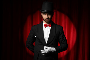 Male magician with wand near red curtain
