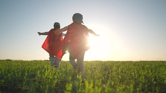 Children superhero cape dash across field. Boy and girl playing outdoor game. Summer light on children cape. Running children pretend superhero on big green field. Boy and girl keep playing together.