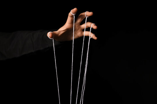 Female hand of puppeteer with strings on dark background