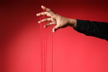 Female hand of puppeteer with strings on red background