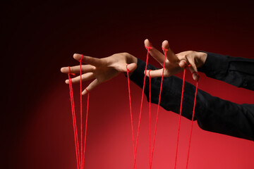 Female hands of puppeteer with strings on dark red background
