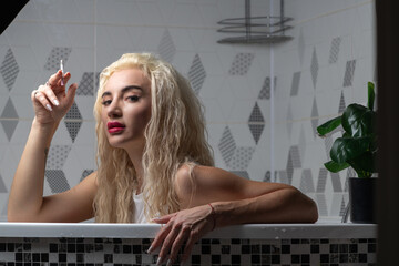 Woman with long blonde hair, relaxing in a bathtub, holding a cigarette, surrounded by modern tiled walls, exuding a sense of calm and contemplation in a serene bathroom setting