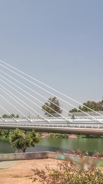 Alamillo Bridge with a tall pylon and steel cables spans over the Guadalquivir River in Seville, Spain. Timelapse hyperlapse of modern suspension design with busy traffic under a clear blue sky.