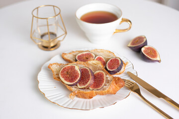 Beautiful and elegant breakfast with cup of tea, croissant with fig on plate and golden candle