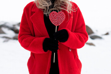 Woman in red coat holding heart lollipop on snow background