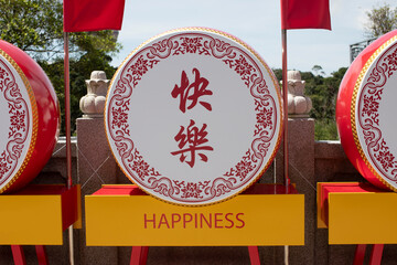 Large circular sign with Chinese characters and decorative elements, mounted on a red stand. The sign has a yellow banner with the word "Happiness" written in red.